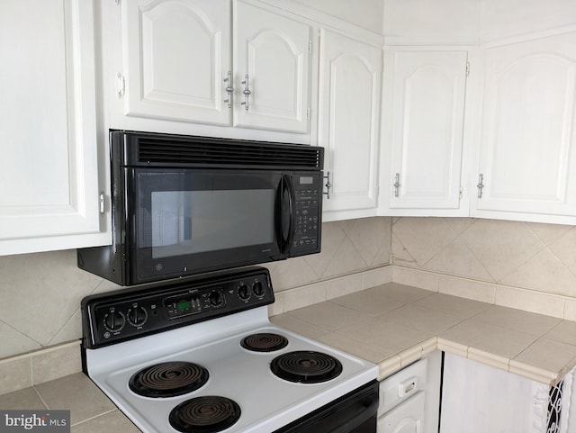 kitchen with range with electric cooktop, tile countertops, black microwave, backsplash, and white cabinets