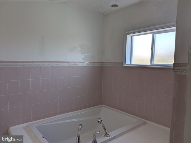 bathroom with a tub to relax in, tile walls, a textured ceiling, and tile patterned flooring