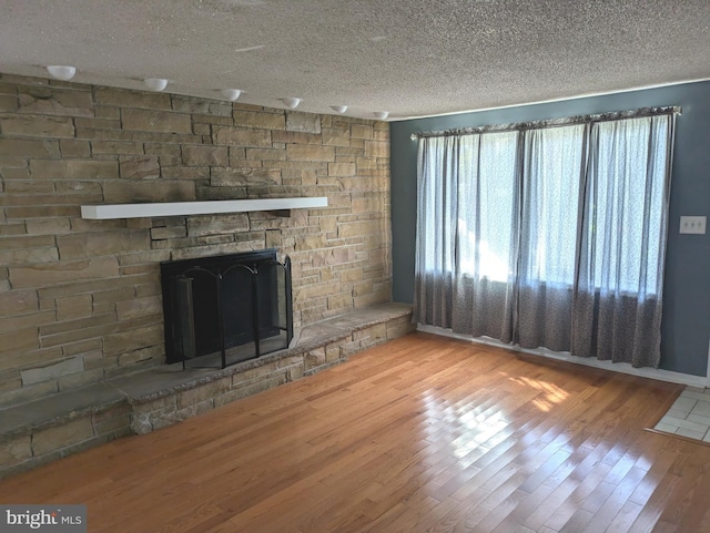 unfurnished living room featuring a textured ceiling, wood finished floors, and a stone fireplace