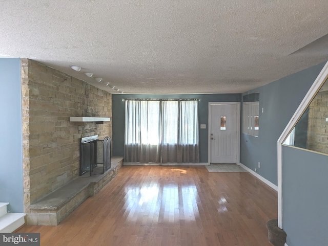 unfurnished living room featuring a textured ceiling, wood finished floors, baseboards, and a fireplace