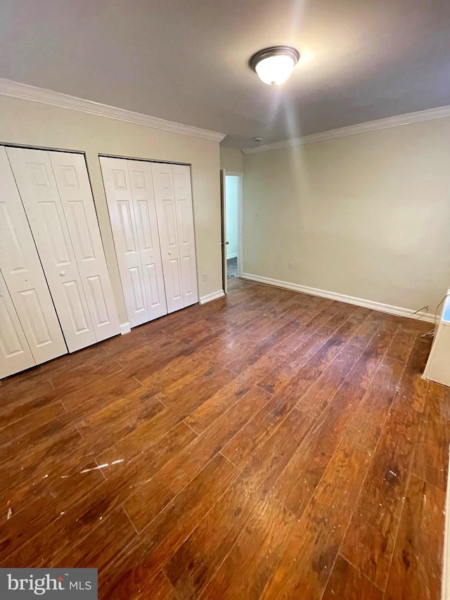 unfurnished bedroom featuring ornamental molding, two closets, and dark hardwood / wood-style flooring