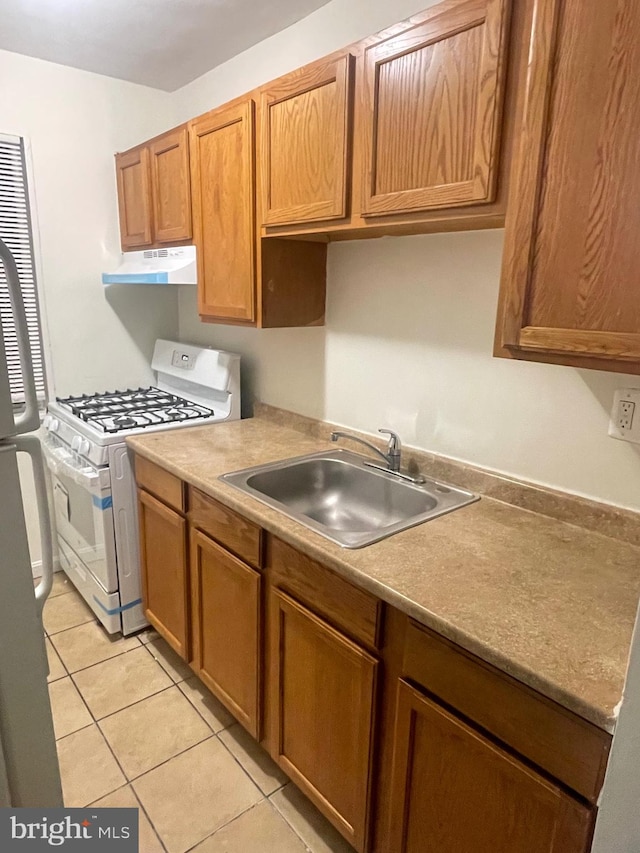 kitchen featuring light tile patterned floors, refrigerator, sink, and white gas stove