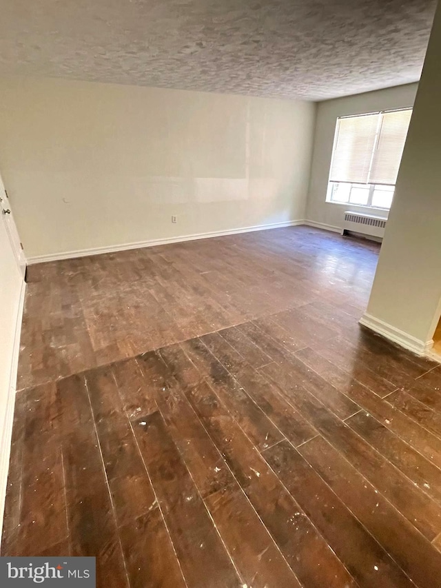 empty room with a textured ceiling, radiator heating unit, and dark hardwood / wood-style flooring