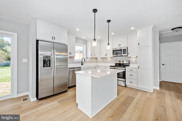 kitchen featuring stainless steel appliances, light hardwood / wood-style floors, white cabinets, and decorative light fixtures