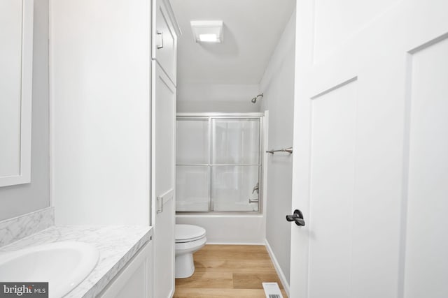 full bathroom with bath / shower combo with glass door, hardwood / wood-style floors, vanity, and toilet