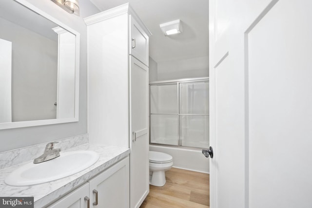 full bathroom featuring wood-type flooring, enclosed tub / shower combo, vanity, and toilet