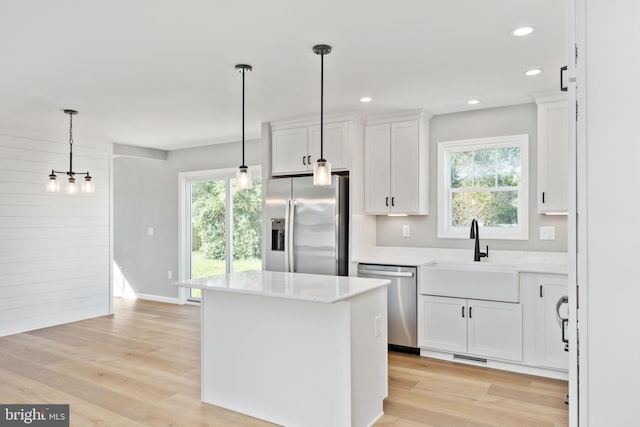 kitchen with pendant lighting, a kitchen island, light hardwood / wood-style flooring, white cabinets, and appliances with stainless steel finishes