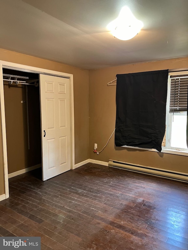 unfurnished bedroom with a closet, dark wood-type flooring, and a baseboard heating unit