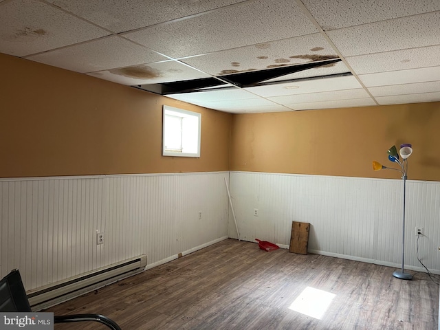 empty room featuring wood-type flooring, a paneled ceiling, a baseboard heating unit, and wood walls