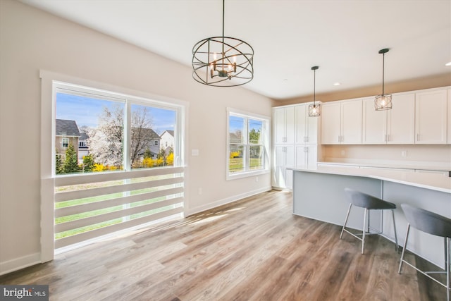 kitchen featuring white cabinets, baseboards, decorative light fixtures, light countertops, and light wood finished floors