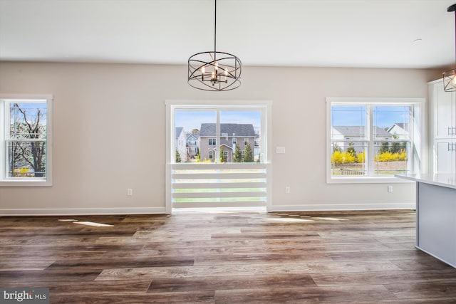 unfurnished dining area with a chandelier, baseboards, and wood finished floors