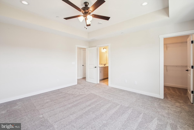 unfurnished bedroom with a spacious closet, a tray ceiling, baseboards, and light colored carpet