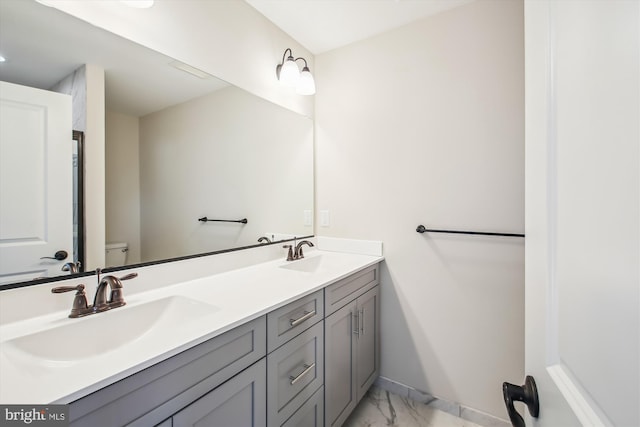 full bath featuring toilet, double vanity, marble finish floor, and a sink
