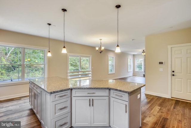 kitchen with wood-type flooring, light stone countertops, and pendant lighting