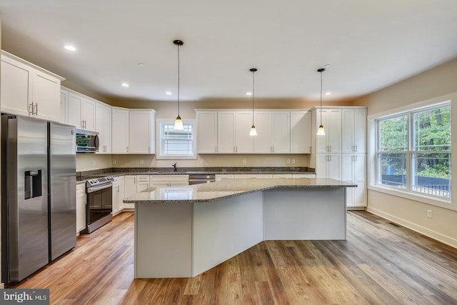 kitchen with decorative light fixtures, white cabinetry, appliances with stainless steel finishes, a center island, and light hardwood / wood-style floors