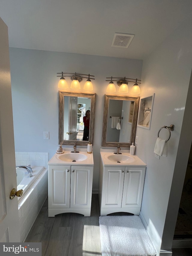 bathroom featuring tiled bath, wood-type flooring, and vanity