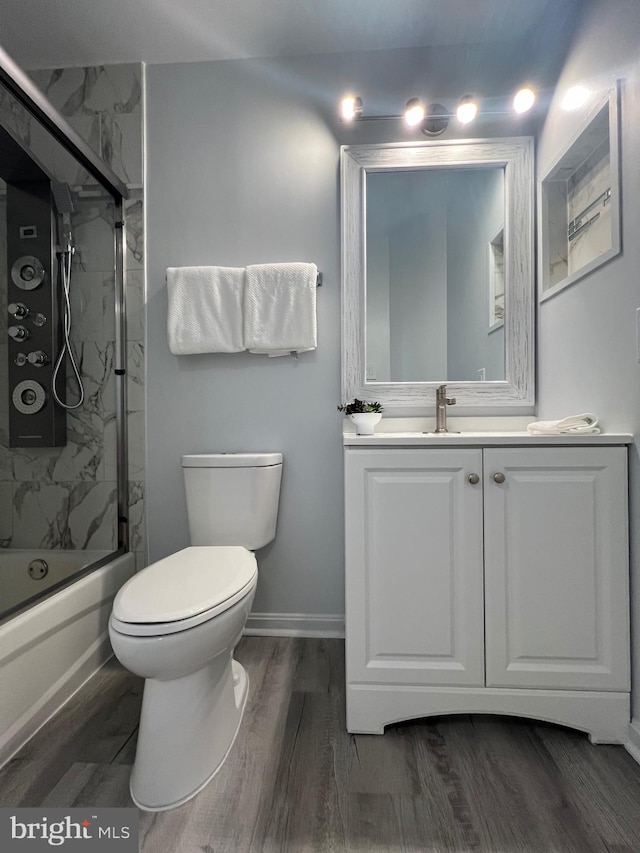 full bathroom featuring hardwood / wood-style flooring, vanity, combined bath / shower with glass door, and toilet