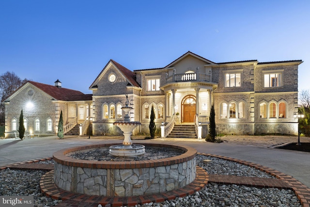 view of front of property featuring brick siding, curved driveway, and a balcony