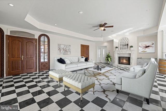 living area featuring recessed lighting, a warm lit fireplace, a raised ceiling, and ceiling fan