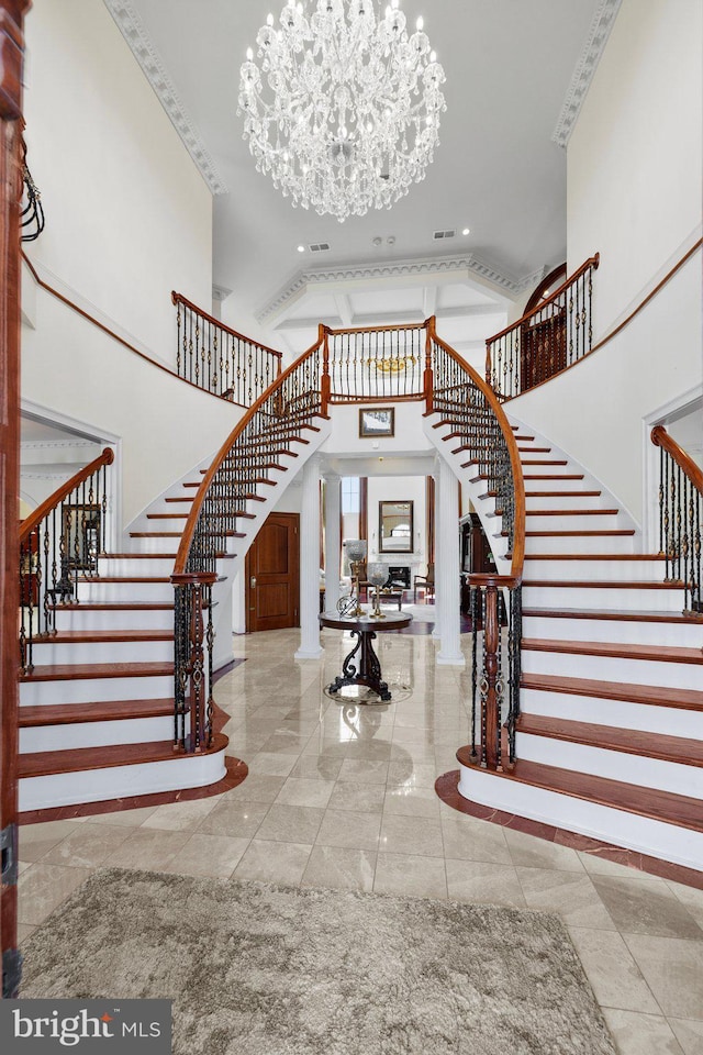 foyer featuring stairs, a chandelier, a towering ceiling, and ornate columns