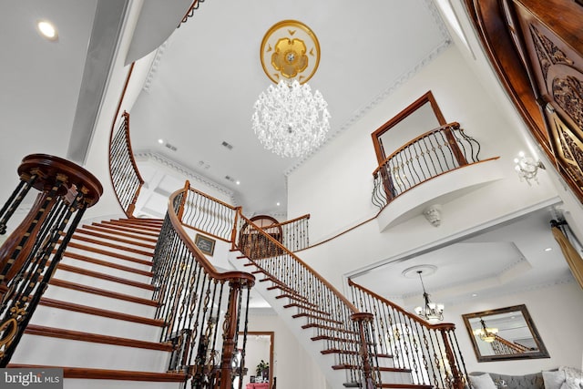 staircase with visible vents, a high ceiling, crown molding, a notable chandelier, and recessed lighting