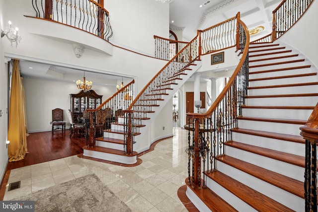 stairway featuring baseboards, visible vents, tile patterned floors, a high ceiling, and a chandelier