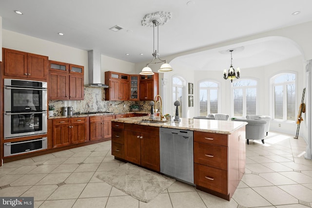 kitchen with a warming drawer, stainless steel appliances, glass insert cabinets, a sink, and wall chimney range hood