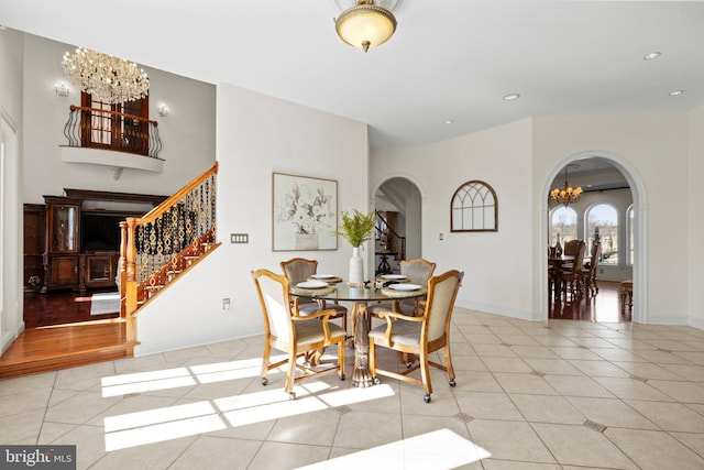 dining space featuring arched walkways, light tile patterned floors, baseboards, stairs, and an inviting chandelier