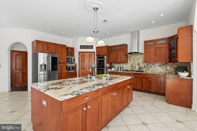 kitchen featuring tasteful backsplash, visible vents, stainless steel appliances, wall chimney range hood, and a sink