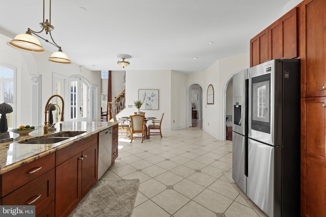 kitchen with light tile patterned floors, arched walkways, appliances with stainless steel finishes, light stone countertops, and a sink