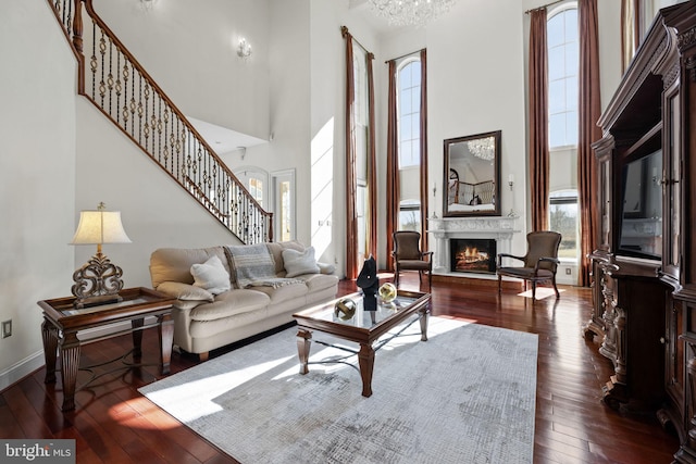 living area with a towering ceiling, baseboards, a lit fireplace, stairway, and dark wood finished floors