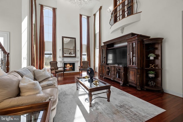 living room featuring a lit fireplace, dark wood finished floors, plenty of natural light, and a towering ceiling