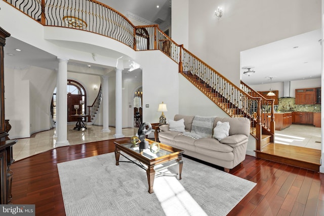 living room with arched walkways, light wood-style floors, a towering ceiling, stairway, and ornate columns