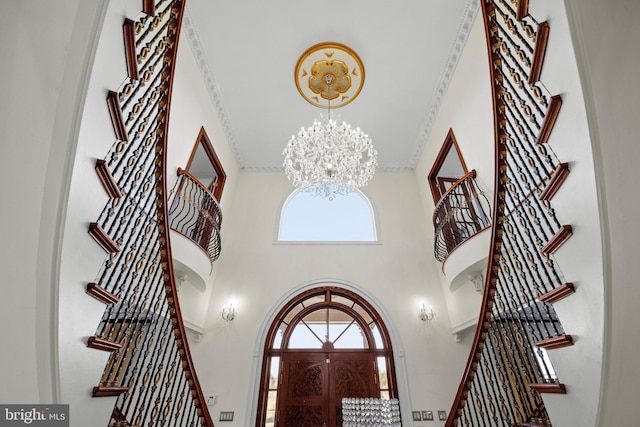 foyer with stairs, ornamental molding, a high ceiling, and a notable chandelier