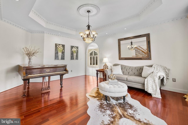 sitting room featuring arched walkways, a tray ceiling, hardwood / wood-style flooring, and an inviting chandelier