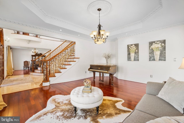 living area with a tray ceiling, a notable chandelier, ornamental molding, hardwood / wood-style floors, and stairs