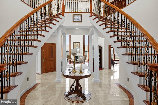 entryway featuring baseboards, decorative columns, and a high ceiling