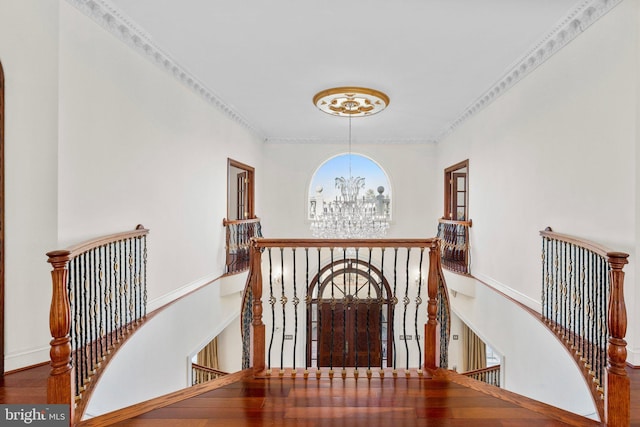 corridor featuring baseboards, wood finished floors, an inviting chandelier, crown molding, and an upstairs landing