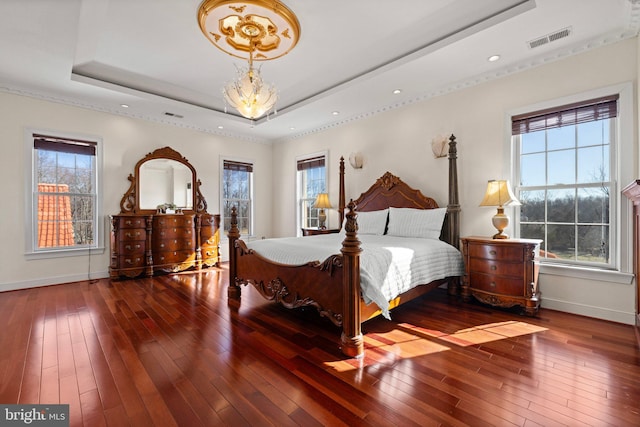 bedroom with wood-type flooring, multiple windows, visible vents, and a raised ceiling