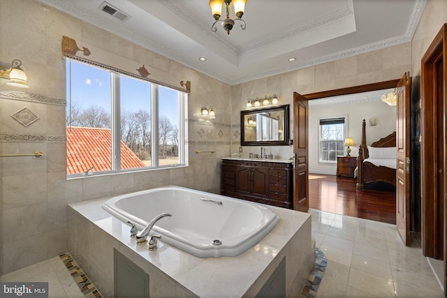 bathroom featuring visible vents, ensuite bathroom, a garden tub, a tray ceiling, and tile walls