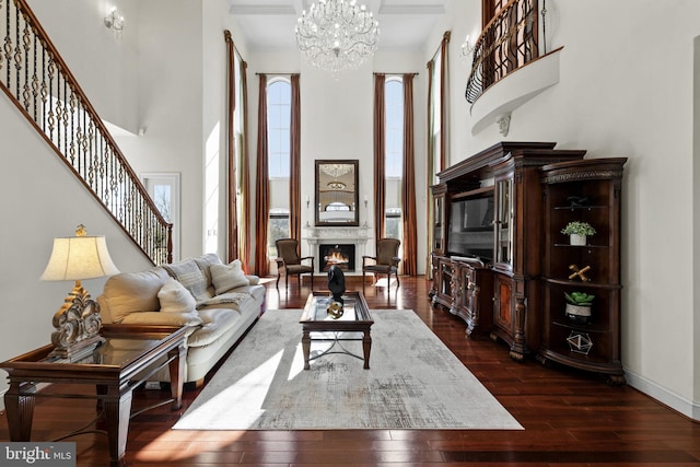 living room with dark wood-style flooring, a towering ceiling, baseboards, stairs, and a lit fireplace