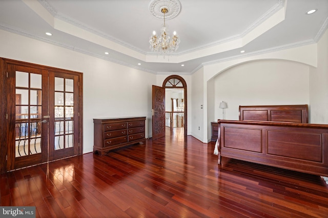 unfurnished bedroom with a notable chandelier, wood finished floors, french doors, a tray ceiling, and crown molding