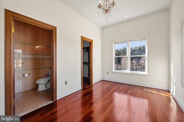 unfurnished bedroom featuring crown molding, a spacious closet, dark wood finished floors, and a notable chandelier