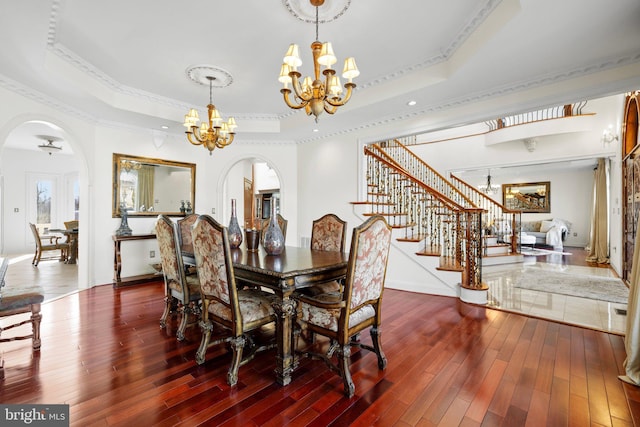 dining area featuring arched walkways, hardwood / wood-style flooring, stairs, a tray ceiling, and a chandelier