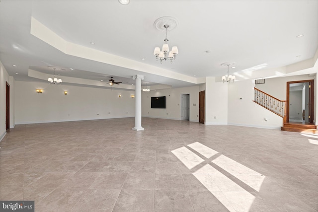 unfurnished living room featuring baseboards, stairway, ornate columns, and ceiling fan with notable chandelier