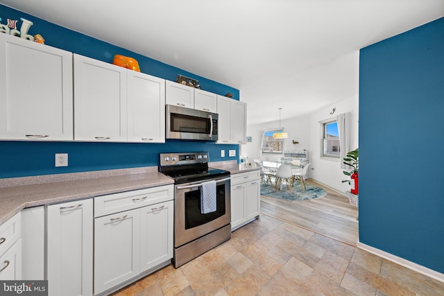 kitchen featuring appliances with stainless steel finishes, hanging light fixtures, white cabinetry, and light hardwood / wood-style floors