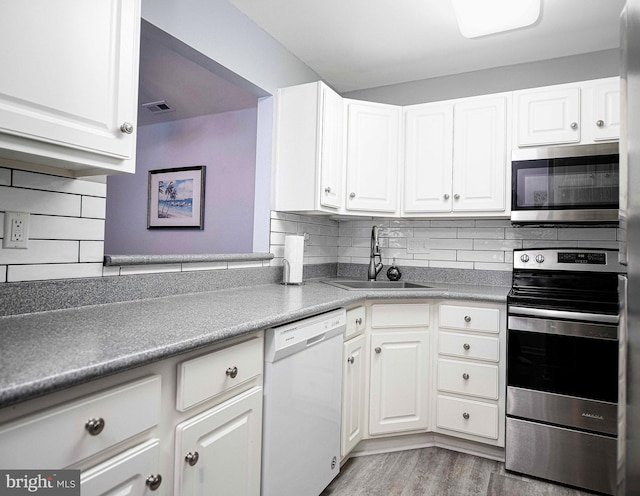 kitchen with appliances with stainless steel finishes, white cabinetry, sink, and backsplash