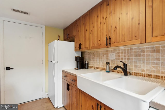 kitchen featuring sink, white fridge, light wood-type flooring, and tasteful backsplash