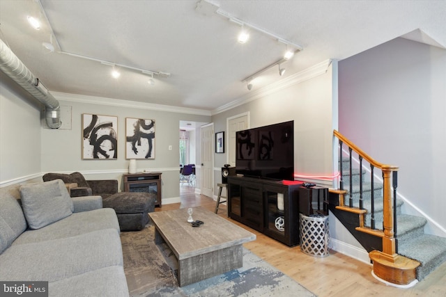 living room with rail lighting, hardwood / wood-style flooring, crown molding, and a fireplace