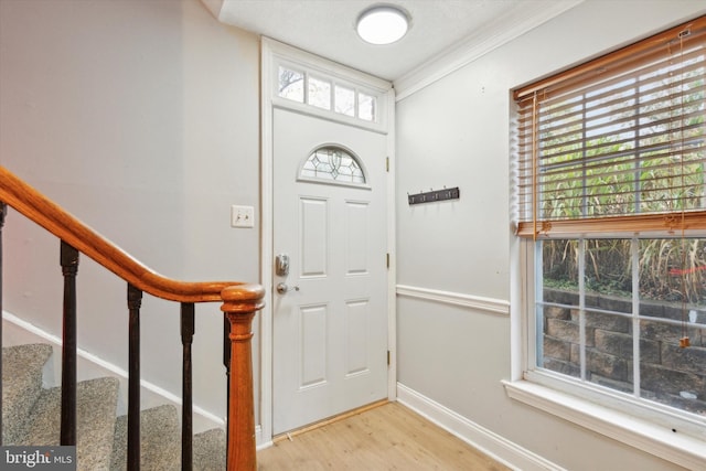 foyer with ornamental molding, light wood-type flooring, and a wealth of natural light